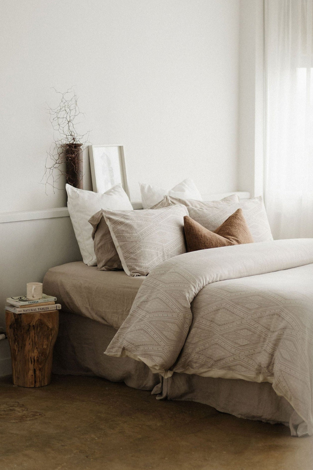 Neatly made bed with beige and white bedding in a softly lit bedroom.